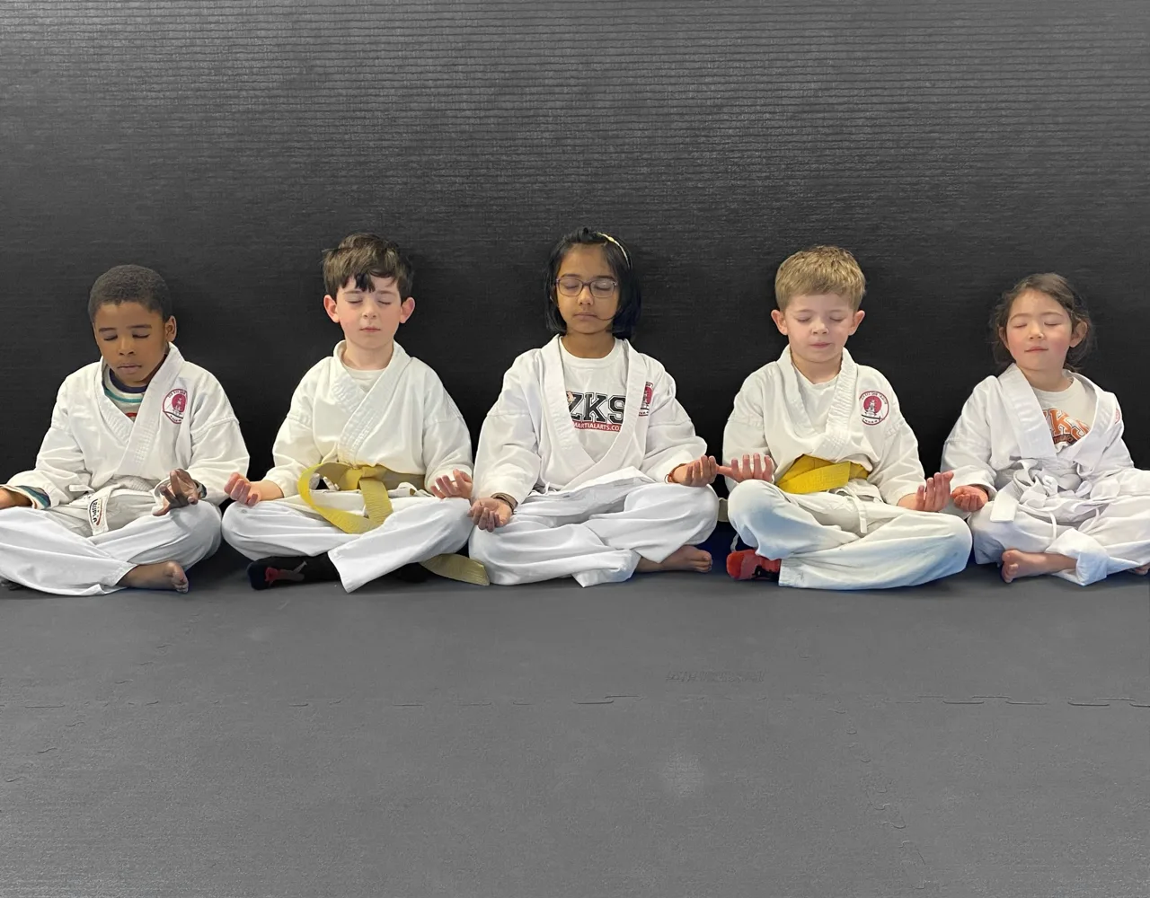 Mini Ninjas children sitting cross-legged with their eyes closed on the mats