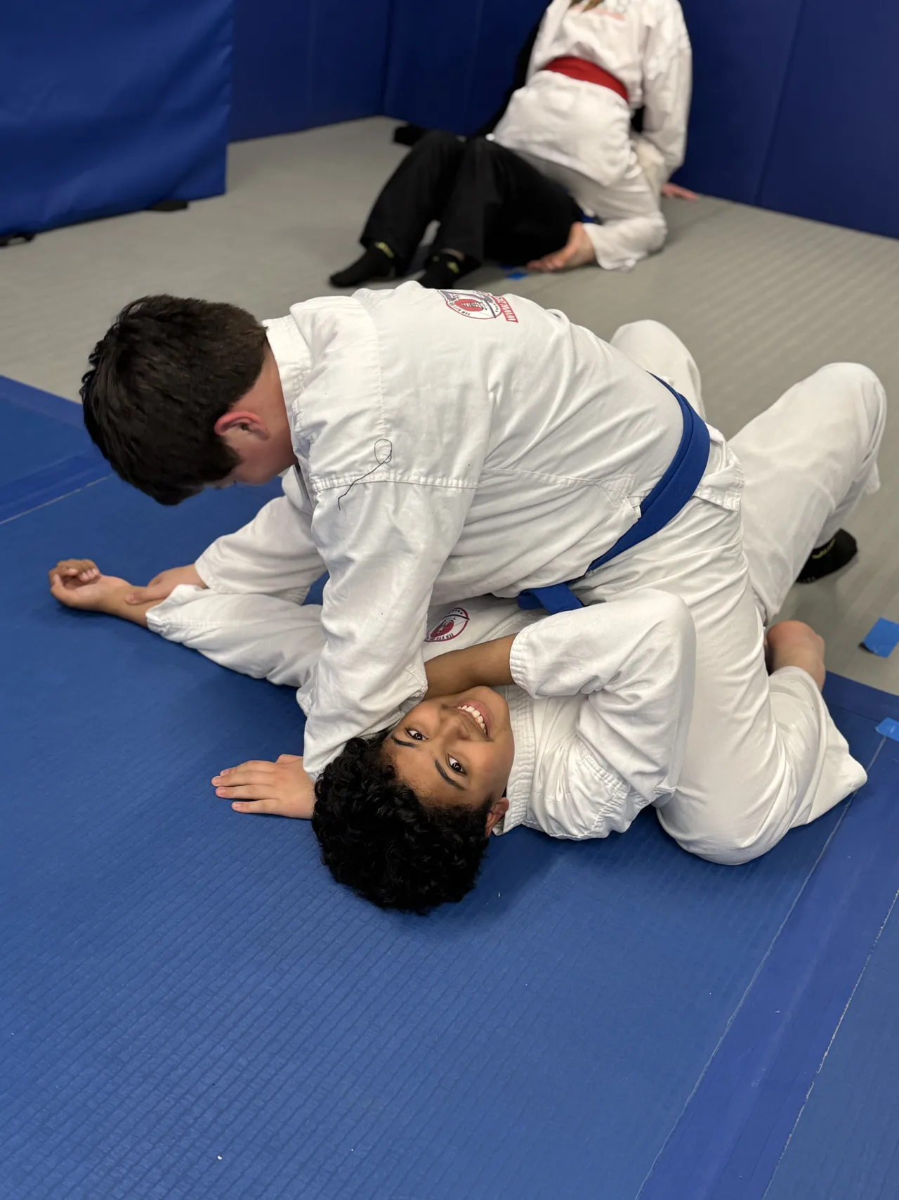 Teen MA students practising a ground position with a partner on padded mats